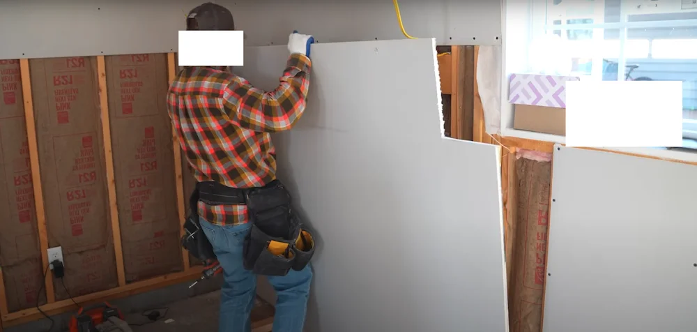 Un homme installant une plaque de cloison sèche sur le mur.