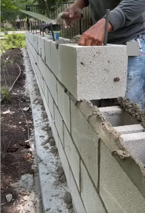 Un homme posant des briques de béton avec du ciment pour construire un mur.